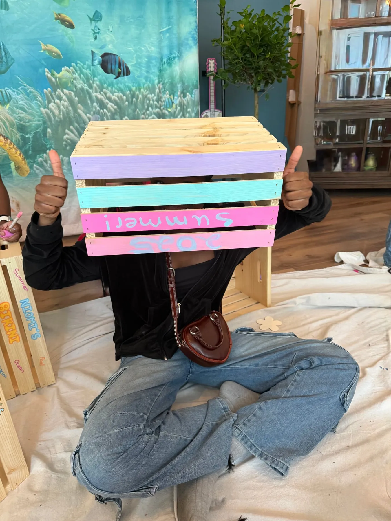 A guest holds up a pastel crate she painted with her name.