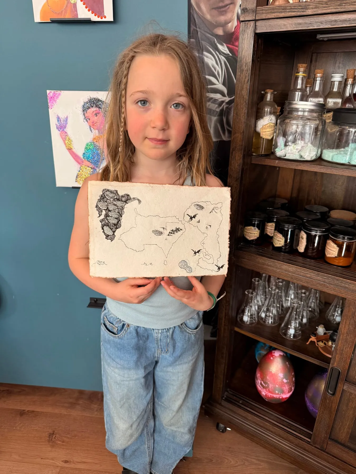 A girl holds up a fantasy map she drew in the studio.