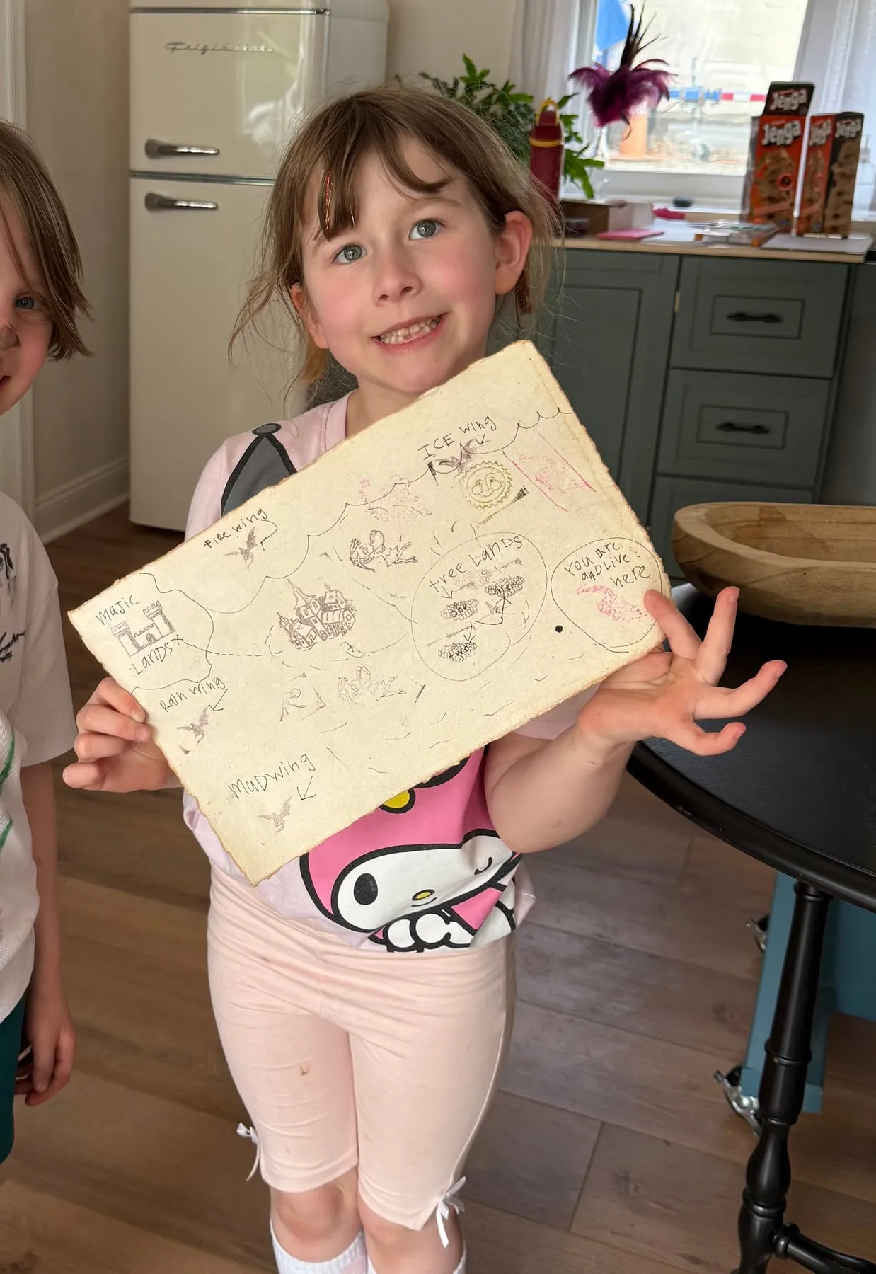 A girl holds up the dragon realm map she drew at a Dragon Keepers party.