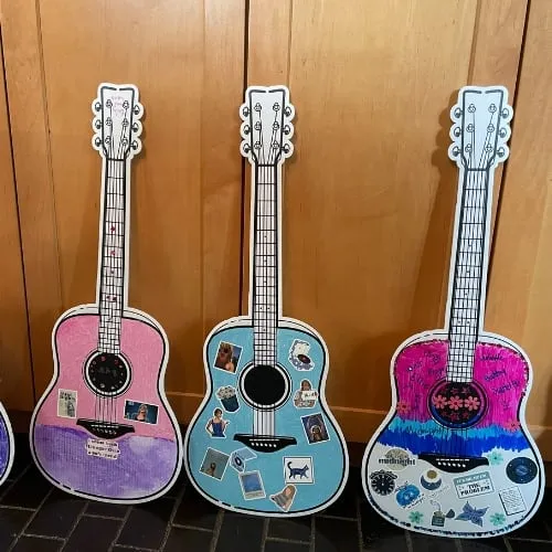 Three decorated guitars from a Taylor Swift party lined up on a bench.
