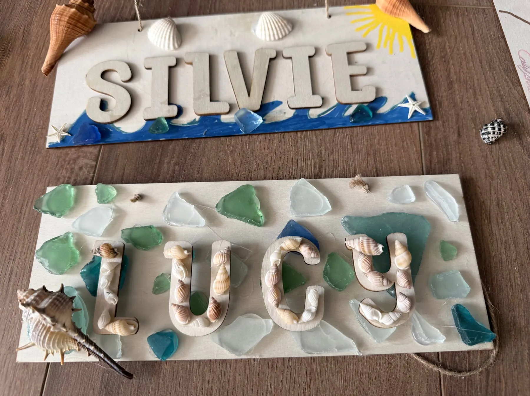 Wooden name signs for Silvie and Lucy decorated with shells and sea glass.